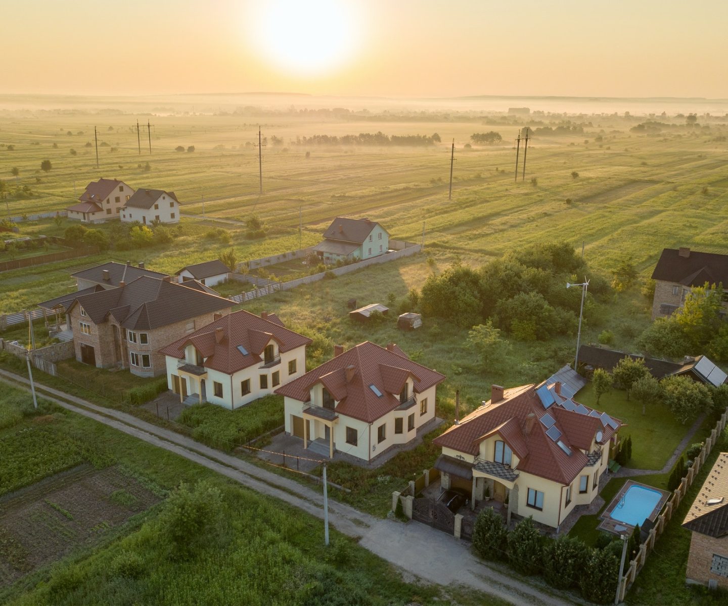 Aerial view of rural residential area with private homes between green fields at sunrise